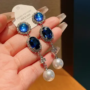 Close-up of elegant vintage blue gem earrings with pearl tassels and high-quality silver pins.