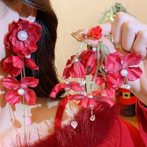 Detailed view of oversized red fabric flower earrings with pearls and crystal drops.