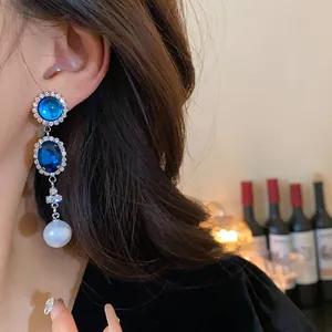 Close-up of vintage French style earrings with blue gemstones and pearl tassel on ear.