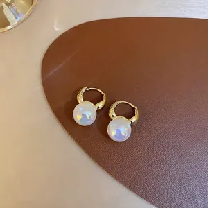 Close-up of elegant gold hoop earrings featuring iridescent mermaid pearls on brown leather.