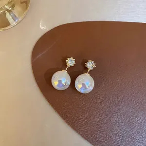 Close-up of mermaid pearl earrings with sparkling rhinestone studs on brown leather.