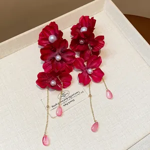 Close-up of elegant red fabric flower earrings featuring pearls and pink teardrop beads.