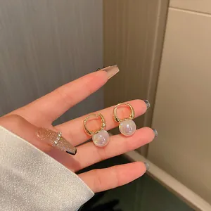 Close-up of mermaid pearl hoop earrings held on fingers showing an elegant iridescent glow
