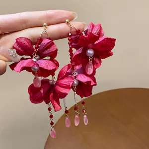 Detailed view of red fabric flower earrings with pearls and long bead tassels