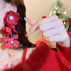 Macro view of long red fabric flower earrings with white pearl accents and gold chains