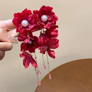 Detail view of oversized red fabric flower earrings with pearls and long tassels.