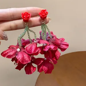 Close-up of red rose stud earrings with green beads and large fabric petals