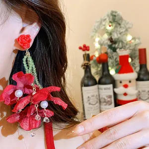 Macro detail view of oversized red fabric flower earrings with pearls and green beads