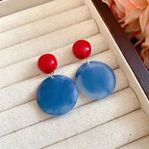 Eleganti orecchini rotondi in acrilico rosso e blu presentati in un portagioie