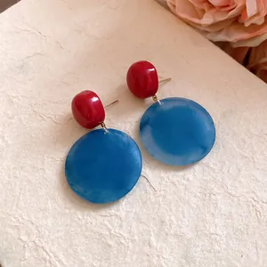 Dettaglio di orecchini tondi in acrilico con contrasto rosso e blu marmorizzato