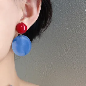 Primo piano di eleganti orecchini rotondi in acrilico rosso e blu indossati su un orecchio