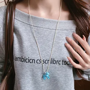 Gros plan d'un pendentif poney en émail bleu porté sur un long collier de pull en cordon