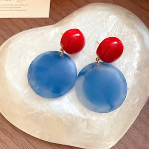 Primo piano di orecchini tondi in acrilico rosso e blu su una base di pietra chiara