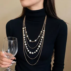 Elegante collar largo multicapa dorado con perlas blancas sobre jersey de cuello alto negro