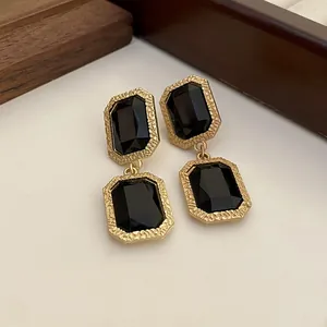 Detailansicht quadratischer schwarzer Kristall-Ohrhänger mit goldfarbenem Rahmen.