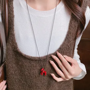 Gros plan d'un pendentif poney rouge sur un collier noir délicat porté sur un pull.