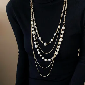 Detalle del elegante collar multicapa de cadena dorada con perlas blancas sobre suéter negro.