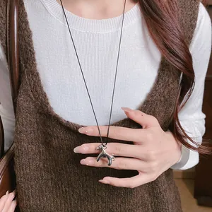 Gros plan d'un pendentif cheval argenté porté sur un gilet en maille blanc et marron.