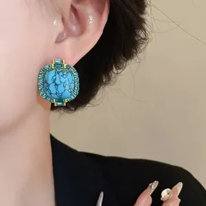 Close-up of a vintage-style gold stud earring with faux turquoise and blue rhinestones.