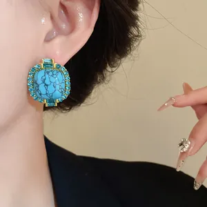 Close-up of vintage faux turquoise stud earrings with blue crystals on model's ear.