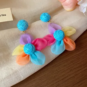 Close-up of vibrant multi-colored chiffon flower earrings with blue raffia studs