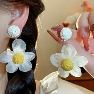 Detail view of handmade chiffon flower earrings with yellow raffia center and white studs
