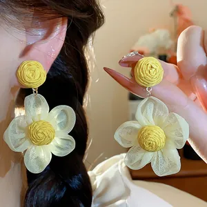 Close-up detail showing the texture of yellow raffia and white chiffon flower earrings