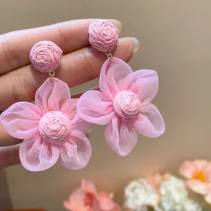 Detailed close-up view of pink raffia and chiffon flower stud earrings held in hand.