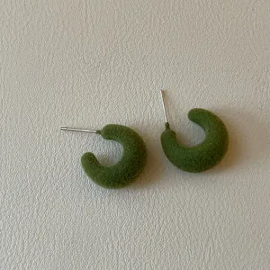 Macro view of green flocked C-shaped stud earrings showing rich velvet texture