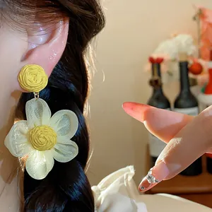 Detailed macro view of yellow raffia and white chiffon floral stud earrings on model