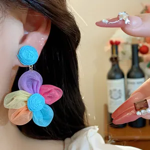 Close-up of colorful raffia and chiffon flower stud earrings worn by a model in detail view.