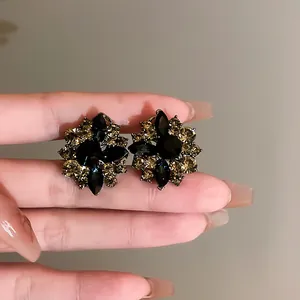 Close-up of vintage flower stud earrings with black and amber crystals on fingers.