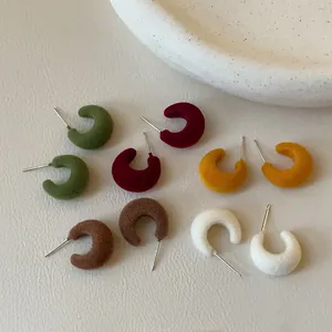 Detail view of five pairs of colorful flocked C-shaped stud earrings in autumnal tones.