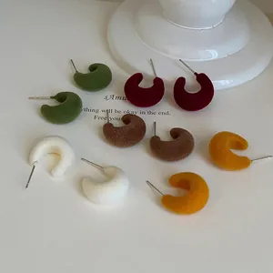 Close-up of minimalist flocked C-shaped stud earrings in various autumn colors