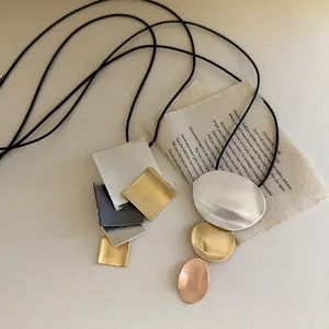 Detail view of a geometric metal pendant necklace with a matte finish on a black cord.