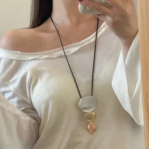 Detail shot of a long geometric metal pendant sweater chain worn with a white off-shoulder top