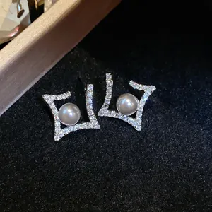 Macro view of elegant silver rhombus stud earrings with pavé zircons and a central pearl