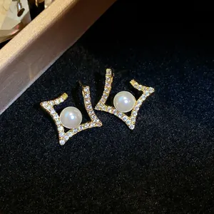 Detailed view of elegant gold geometric earrings with a central pearl and pavé.