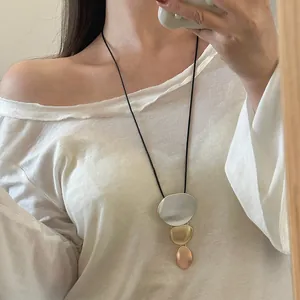 Detailed view of a geometric three-tone metal pendant necklace worn on a white top