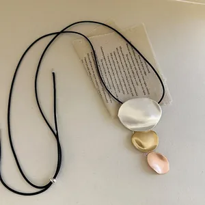 Close-up detail of geometric metal pendant necklace featuring a three-tone metallic finish.