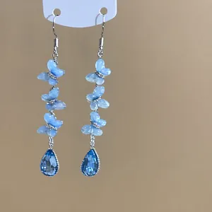 Dettaglio ravvicinato di orecchini a nappa con farfalle in tessuto blu e perline.