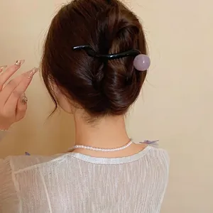 Elegant minimalist black wave hair clip with purple resin ball shown on model's bun hair.