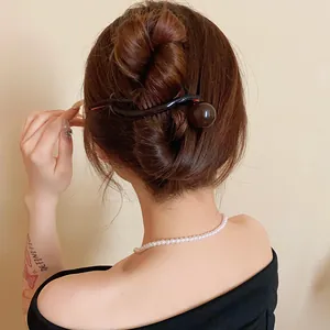 Close-up detail of a minimalist round resin hair clip styled on a brown bun hairstyle.