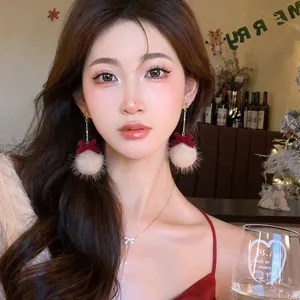 Festive Christmas red velvet bow and white plush ball dangle earrings on model