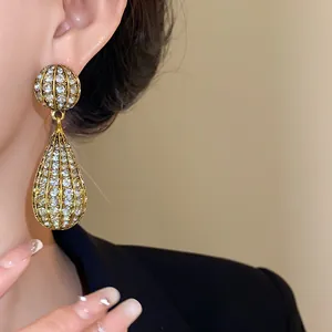 Dettaglio di un orecchino a goccia dorato esagerato con pavé di cristalli