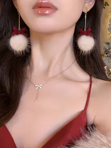 Close-up of festive white plush ball earrings and sparkling bow necklace on a model.