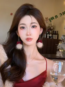 Close-up view of elegant Christmas plush ball and red bow drop earrings on model's ear