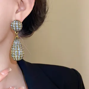 Eleganti orecchini a goccia dorati con strass scintillanti indossati dal modello.
