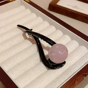 Close-up of black duckbill hair clip with large pink resin bead on velvet box