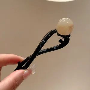 Close-up view of a black resin hair clip with a cream-colored round bead detail.